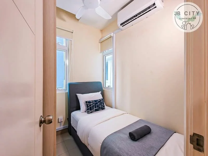 Bedroom features: single bed with grey upholstered headboard, white bedding, decorative pillow with geometric pattern, grey towel rolled on bed, light beige painted walls, floor-to-ceiling window, white sheer curtains, wall-mounted split AC unit, ceiling fan, tile flooring; style: modern.