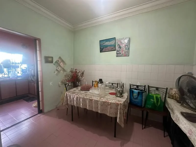 Dining features: green painted walls, white tiled backsplash, pink tile flooring, dining table with tablecloth, four dining chairs, wall-mounted fan, decorative wall art, plastic shopping bags, glass vase with dried flowers. Kitchen features: white cabinetry, stainless-steel sink, kitchen countertop, kitchen appliances visible.