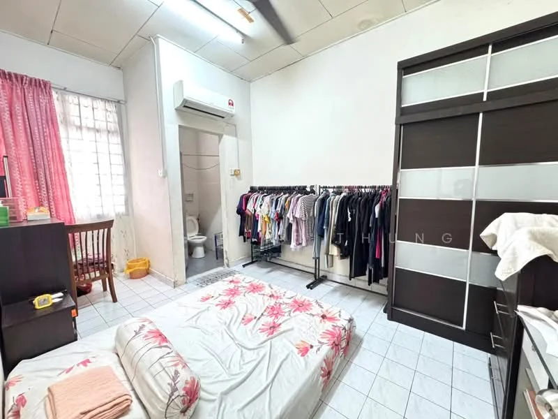 Bedroom features: single bed with floral bedding, floor-to-ceiling window with sheer curtains, 1 wall-mounted split AC, white tiled flooring, light grey painted walls, clothes rack with hanging clothes, wooden dining table with chair, built-in wardrobe with sliding doors, open space for movement, toilet visible in the background; style: minimalist.