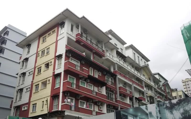 Exterior type: low-rise apartment block; features: red and cream painted facade, balconies with railings, multiple air conditioning units visible, flat roof, approximately 5-storey building, windows with grilles, exposed concrete elements; style: modern.