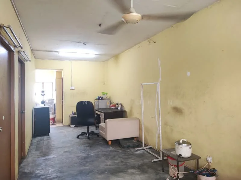Room features: yellow painted walls, concrete flooring, ceiling fan, desk with chair, computer workstation, doorway leading to another room, visible electrical outlets, unpainted wall section, small white stand, kitchen appliance on floor.