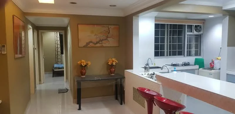 Kitchen features: white countertop, stainless-steel sink, chrome pull-down faucet, built-in gas stove, wall-mounted split AC, white cabinetry, window with grid pattern, green plastic chair; style: modern. Dining features: bar stools, decorative vase with flowers, wall-mounted artwork, cream painted walls, recessed ceiling lights; style: modern. Hallway features: cream painted walls, doorway leading to bedrooms, light-colored flooring.