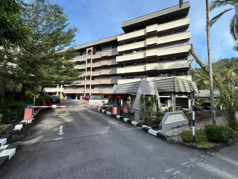 Exterior type: low-rise apartment block; features: 5-storey building, grey painted facade, balconies with railings, manicured landscaping, paved driveway, entrance gate with barrier, surrounded by trees, parking area visible; style: modern.