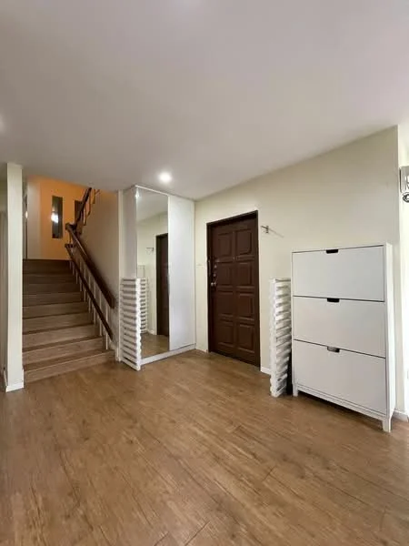 Room features: wooden flooring, white painted walls, mirror on wall, brown wooden door, staircase with wooden railing, white storage cabinet, ceiling lights; style: modern.