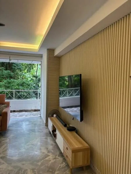 Living features: wall-mounted TV, wooden TV console, strip lighting on ceiling, textured wall with vertical stripes, marble flooring, large windows with view of greenery, sofa, decorative plants; style: modern; view: garden.