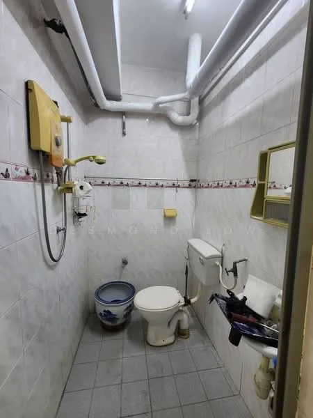 Bathroom features: white tiled walls, grey tiled flooring, toilet, wall-mounted sink, shower with handheld showerhead, water heater, toilet paper holder, small wall-mounted shelf, decorative border tile, exposed plumbing.
