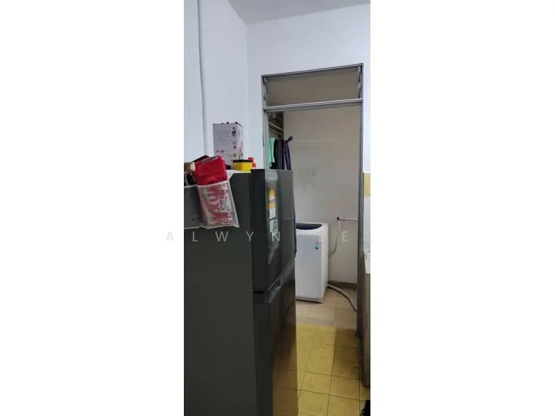 Kitchen features: grey refrigerator, white washing machine, yellow vinyl flooring, white walls, open shelving, cabinets above countertop, countertop, doorway leading to another room.
