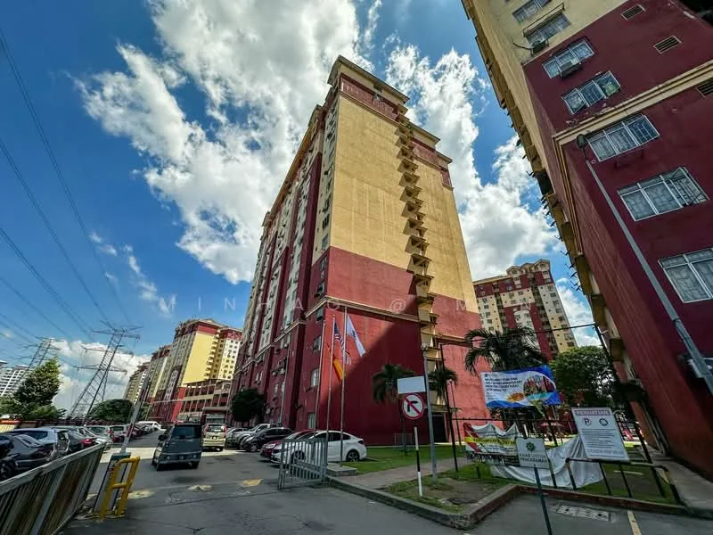 Exterior type: high-rise condominium; features: red and beige painted facade, approximately 10-storey high-rise, surrounded by landscaped greenery, visible parking area, entrance gate with security, flag poles with flags, signage at entrance, power lines visible in foreground; style: modern.