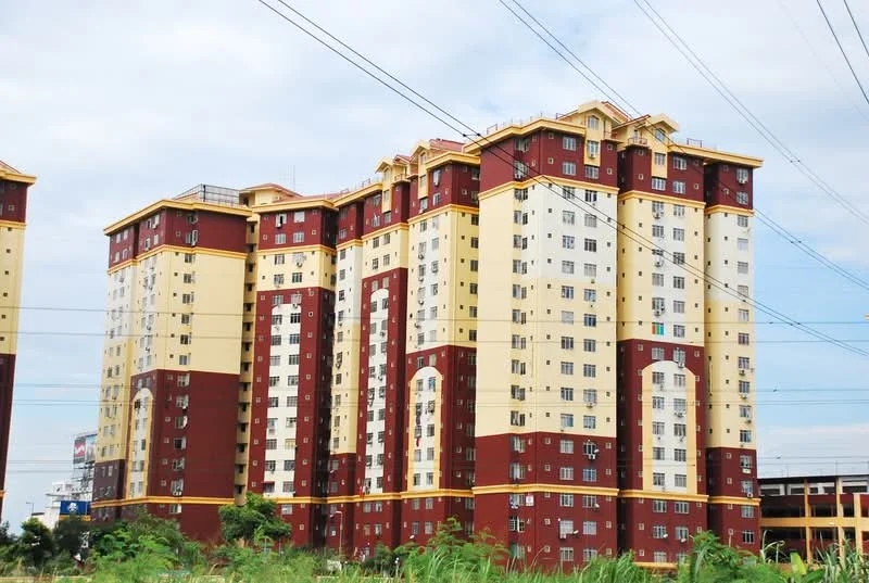 Exterior type: mid-rise condominium; features: red and cream painted facade, multiple storeys, balconies on upper floors, large windows, visible electrical wiring, surrounding greenery, urban context; style: modern.