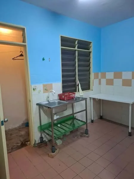 Kitchen features: blue painted walls, white tiled backsplash, cream and brown checkered wall tiles, stainless-steel work table, green shelving unit, single-bowl stainless-steel sink, window with louvered shutters, tile flooring in beige, doorway leading to another room, hanging hook for clothes.