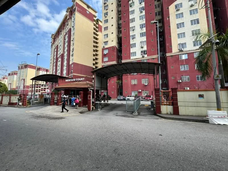 Exterior type: mid-rise condominium; features: red and cream painted facade, main entrance gate, covered entrance with awning, security guard house at entrance, visible parking area, surrounded by mature greenery; style: modern.