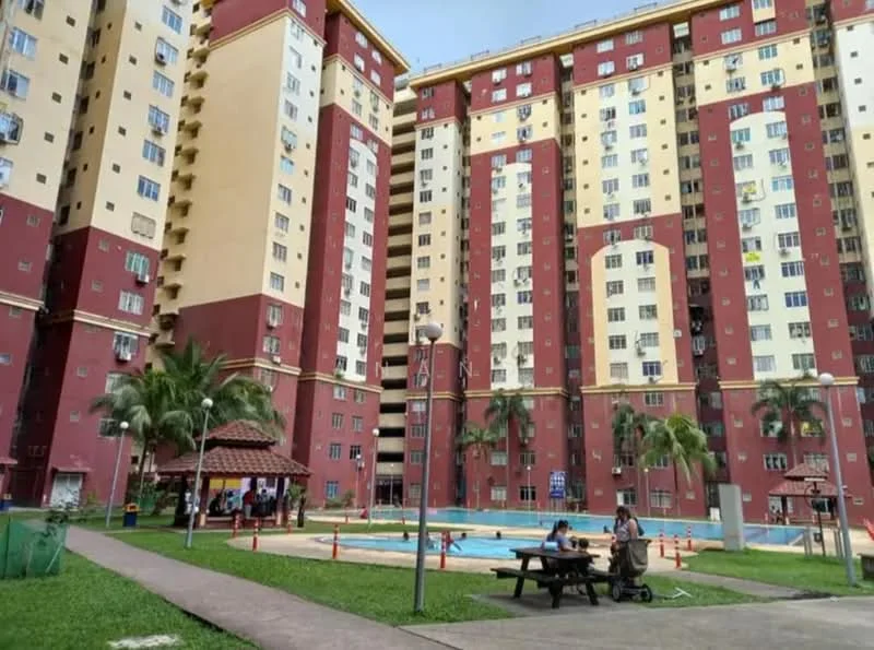 Exterior type: high-rise condominium; features: red and cream painted facade, multiple storeys, swimming pool visible, landscaped garden with grass, palm trees, gazebo, outdoor seating area, walkway, security lighting, surrounded by greenery; style: modern.