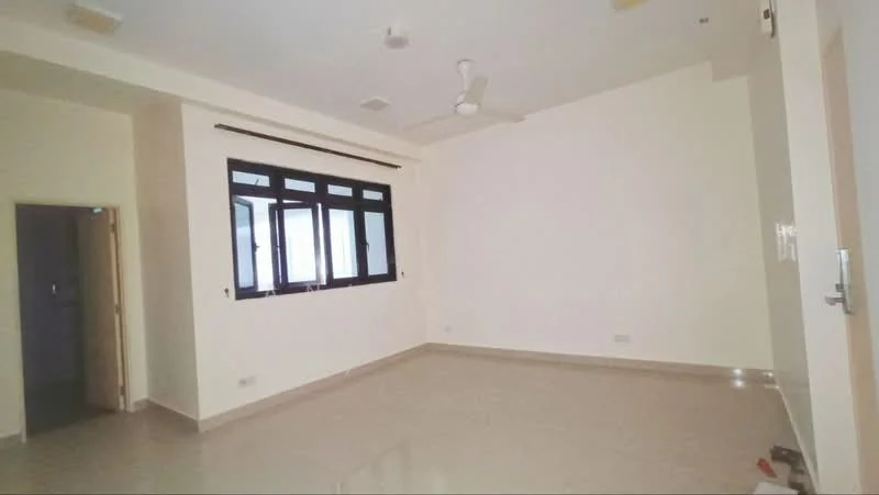 Room features: cream painted walls, polished floor tiles, 5-blade ceiling fan, large windows with black frames, natural light from windows, no visible furniture, neutral color scheme, corner of room visible, doorway leading to another room; style: modern.