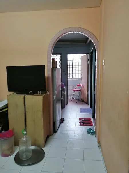 Room features: orange painted walls, white tiled flooring, archway entrance, television on wooden cabinet, refrigerator, plastic chair, doorway leading to another room, floor mat, water bottle, metal tray.