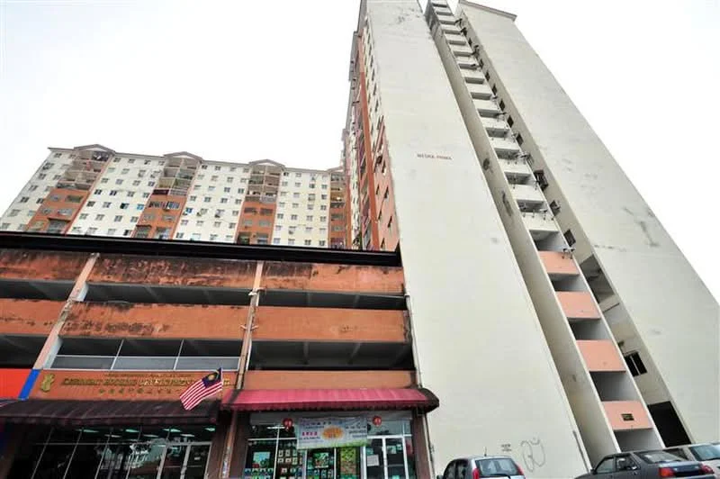 Exterior type: mid-rise condominium; features: multi-storey building, commercial space on ground floor, balconies on upper floors, painted concrete facade, visible signage on commercial unit, parking area beneath building, flag of Malaysia, residential units above commercial space; style: modern.