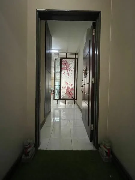 Room features: glossy white tile flooring, cream painted walls, wooden doors, decorative wall with floral pattern, glass partition, recessed lighting, door frame with dark wood finish, green carpet at entrance; style: modern.