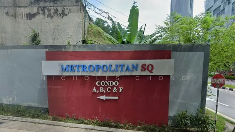 Exterior type: condominium; features: signage with 'METROPOLITAN SQ', red and white color scheme, arrow pointing left, surrounding greenery, paved walkway, adjacent road, nearby high-rise buildings; style: modern.