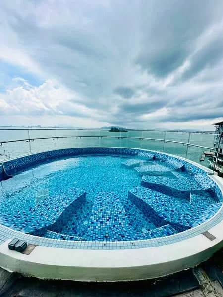 Exterior type: swimming pool deck; features: round infinity pool, blue mosaic tile, water jets, glass railing, ocean view, skyline in background, sun loungers area, decking around pool; style: modern.