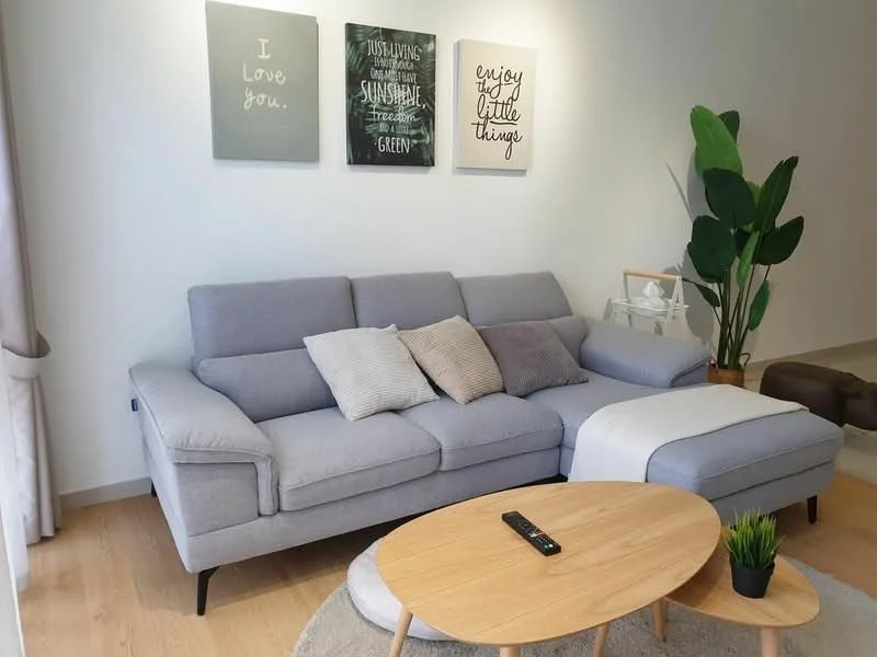Living features: L-shape sectional sofa in grey, decorative throw pillows, round wooden coffee table, area rug, framed artwork on walls, indoor plant, light wood flooring, curtains, wall-mounted decor, neutral wall color; style: modern.