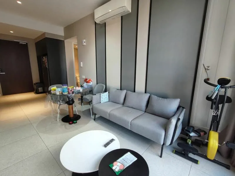 Living features: grey fabric 3-seater sofa, round black coffee table, glass dining table with clear chairs, wall-mounted split AC, light grey painted walls, tile flooring, decorative cushions, exercise equipment, refrigerator visible in background; style: modern.