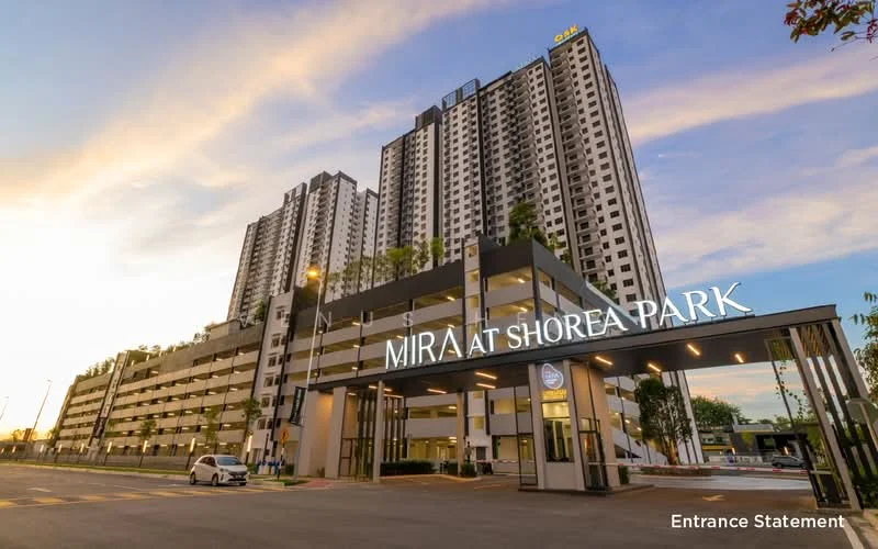 Exterior type: high-rise condominium; features: modern facade with glass and concrete, multiple storeys, entrance statement with signage, landscaped entrance area, parking deck visible, surrounded by greenery, outdoor lighting, driveway access; style: modern.