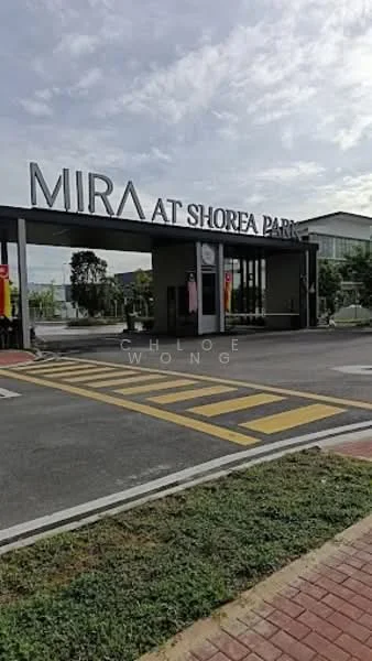 Exterior type: gated community; features: modern entrance gate, signage with 'MIRA AT SHOREA PARK', paved driveway, landscaped greenery, surrounding trees, pedestrian walkway, traffic markings, parking area, security booth, visible residential buildings in background; style: modern.