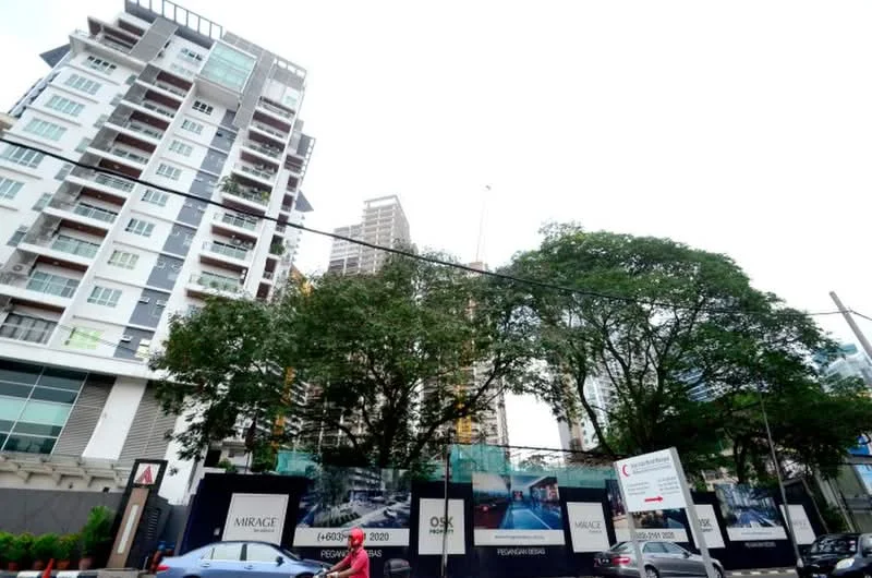 Exterior type: high-rise condominium; features: glass curtain wall, white painted facade, recessed balconies, surrounded by mature greenery, construction site with hoarding, urban context with nearby buildings; style: modern.