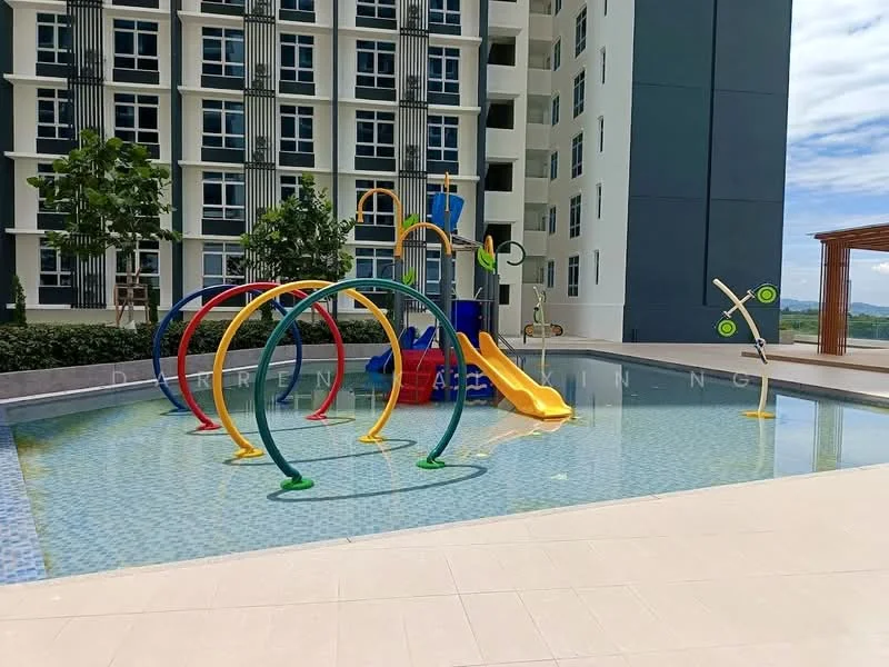 Exterior type: swimming pool deck; features: children's water play area with colorful slides, water spray features, shallow pool area, surrounding landscaped greenery, tiled pool deck, sunny outdoor environment, modern design elements, adjacent building with vertical lines; style: modern.