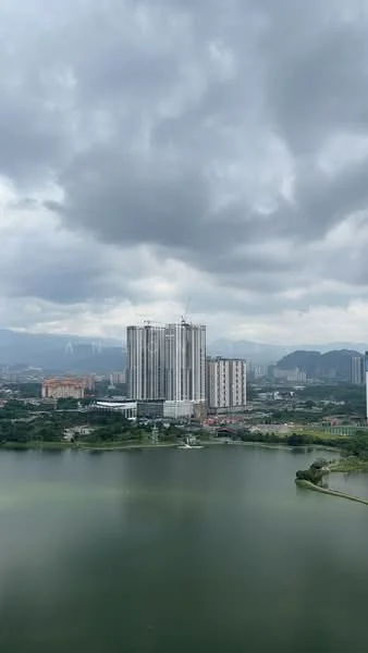 Exterior type: high-rise condominium; features: glass curtain wall, approximately 20-storey high-rise, surrounded by water body, urban skyline in background, green landscaping, construction cranes visible; style: modern.