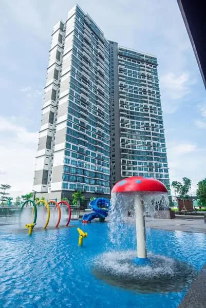 Exterior type: high-rise condominium; features: glass curtain wall, projecting balconies, swimming pool with water features, children's splash area with water slides, colorful water play structures, manicured landscaping, surrounded by greenery; style: modern.
