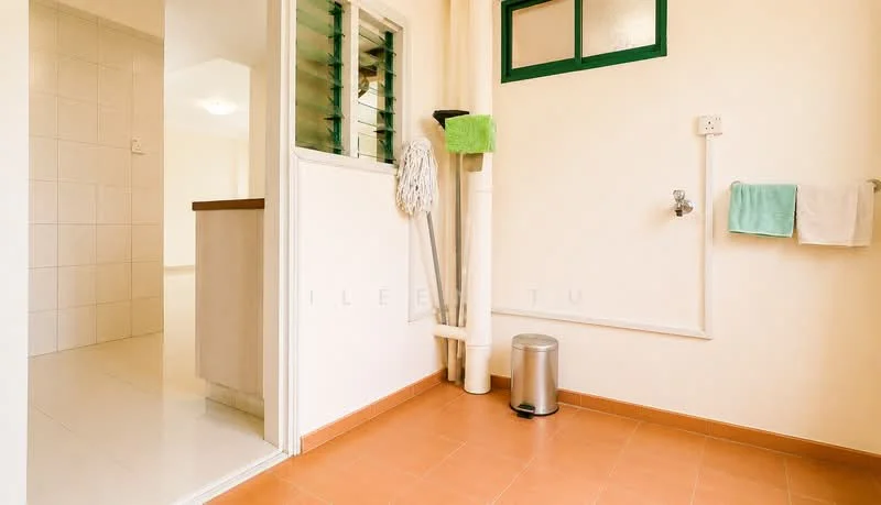 Laundry features: orange ceramic tile flooring, white painted walls, green window with louvered shutters, wall-mounted faucet, mop and cleaning supplies, metal trash can, towel rack with two towels, plumbing pipes visible. Room features: white tiled flooring, white painted walls, open doorway leading to another room.