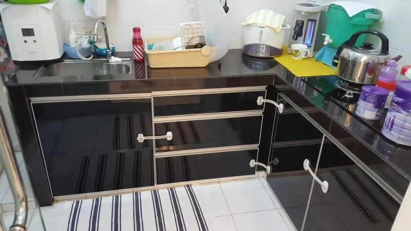 Kitchen features: black laminate cabinetry with stainless-steel handles, single-bowl stainless-steel sink, chrome pull-down faucet, black countertop, white tiled backsplash, built-in stove, kettle, plastic storage containers, dish rack, various kitchen utensils, striped area rug; style: modern.