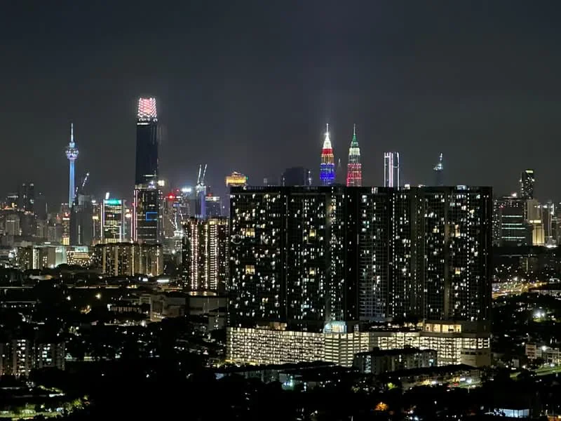 Exterior type: high-rise condominium; features: city skyline view, night lighting, modern architectural design, glass facade, surrounded by urban landscape, prominent landmarks visible, illuminated buildings, multi-storey structure; style: modern.