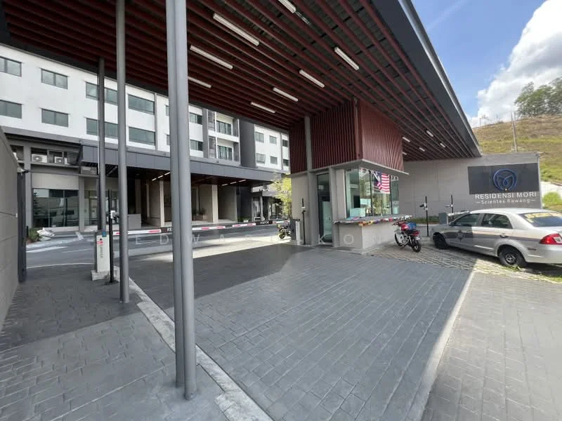 Exterior type: serviced apartment; features: modern facade with horizontal slats, glass entrance, security guard station, automatic barrier gate, paved driveway, landscaped area, parking spaces, signage for 'Residensi Mori', bicycle parking, surrounding greenery; style: modern.
