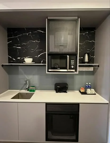 Kitchen features: single-bowl stainless-steel sink, chrome pull-down faucet, black marble backsplash, white countertop, built-in microwave, black toaster, kettle in silver, open shelving, grey cabinetry with mesh front, 2 bottles of water, small dish with snacks; style: modern.
