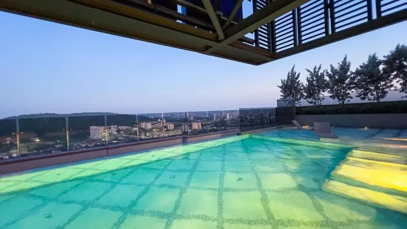 Exterior type: swimming pool deck; features: infinity pool, glass railing, landscaped area with trees, city skyline view, pool deck with loungers, night lighting; style: modern.