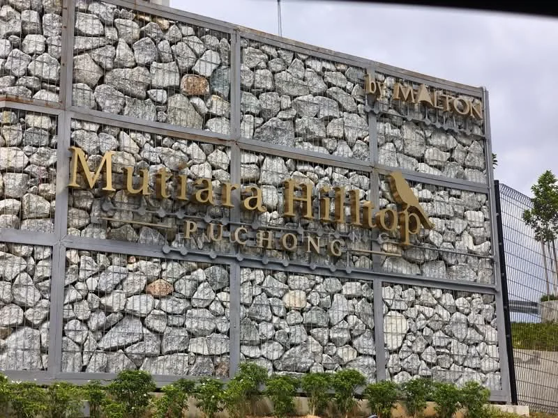 Exterior features: stone cladding, metal frame, landscaped greenery, signage with gold lettering, decorative stone wall, modern architectural design; style: modern.