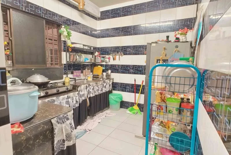 Kitchen features: black marble countertop, stainless-steel gas stove, stainless-steel fridge, white cabinets with black handles, blue and white tiled backsplash, grey tiled flooring, window with black frame, kitchen sink, dish rack, cleaning supplies, decorative items on shelves.