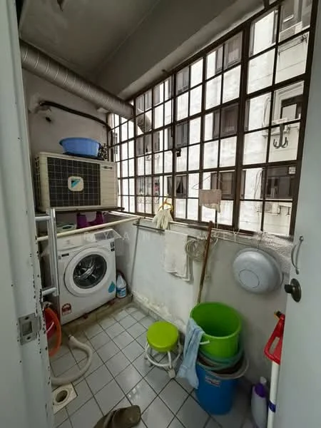 Laundry features: front-load washing machine, window with metal grilles, white tiled flooring, exposed ducting, plastic storage buckets in green and blue, cleaning supplies, small stool, hanging rod for drying clothes.