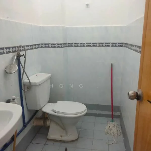 Bathroom features: white toilet, chrome basin mixer faucet, white sink, blue plumbing pipes, blue and white tiled walls, grey floor tiles, mop, cleaning supplies, wall-mounted shower head, decorative border tile.
