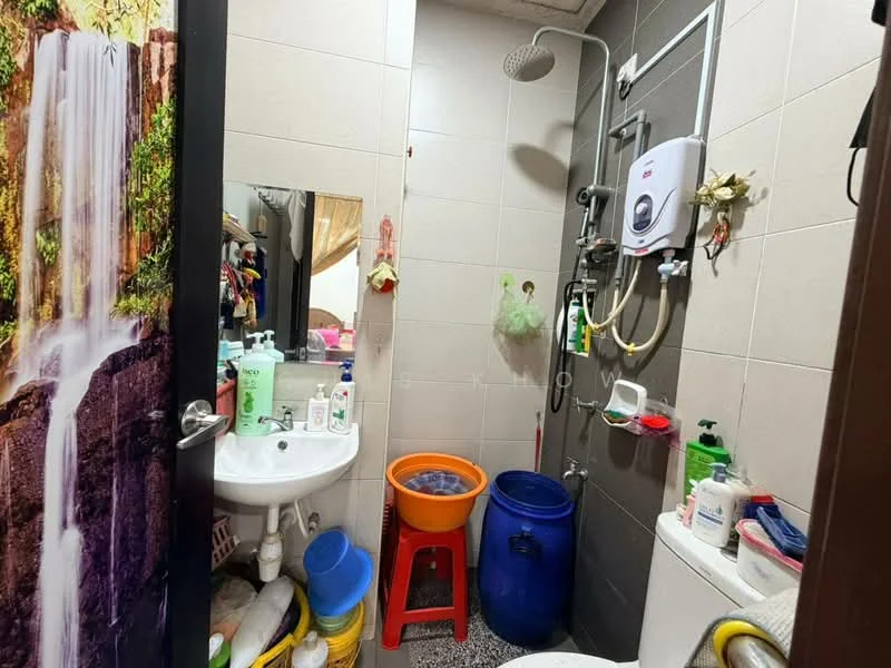 Bathroom features: shower head, wall-mounted water heater, white sink, chrome faucet, mirror, toilet, grey tiled walls, black accent wall, flooring with speckled pattern, cleaning supplies, bucket, blue storage container.