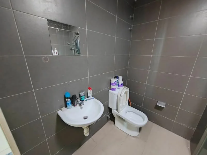 Bathroom features: grey tiled walls, light beige tiled flooring, wall-mounted mirror, single-sink vanity, white toilet, toilet paper holder, various toiletries on sink, shower head visible on wall; style: modern.