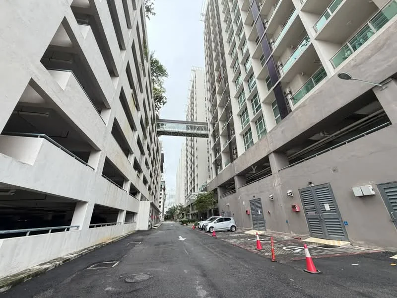 Exterior type: mid-rise condominium; features: multi-storey car park, covered parking, pedestrian bridge connecting buildings, concrete facade, grey painted facade, surrounded by urban landscape, driveway with interlocking pavers, security access points; style: modern.