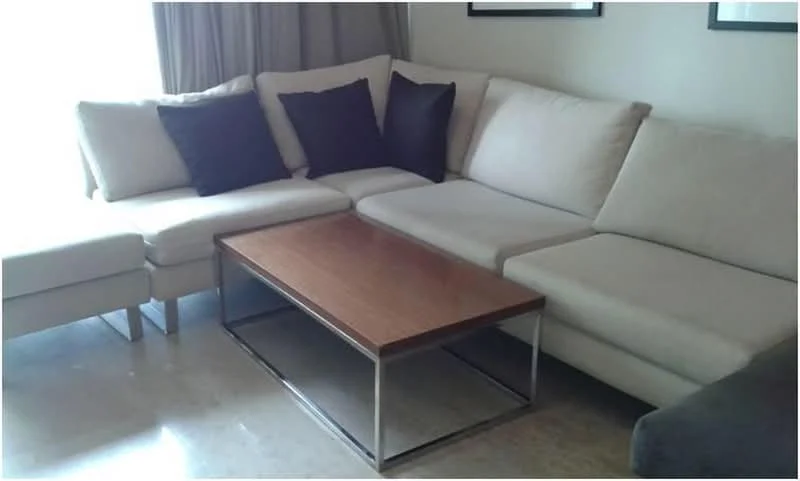 Living features: L-shape sectional sofa in light beige, black throw pillows, wood coffee table with metal frame, marble flooring, floor-to-ceiling window with sheer curtains, neutral wall color, decorative wall art, curtains; style: modern.