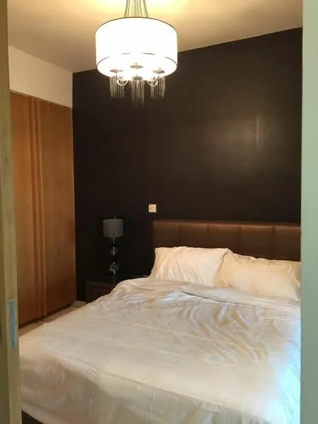 Bedroom features: king-size bed with white bedding, upholstered headboard in brown, wooden wardrobe with sliding doors, nightstand with lamp, chandelier light fixture, dark accent wall, neutral-colored walls, carpeted flooring; style: modern.