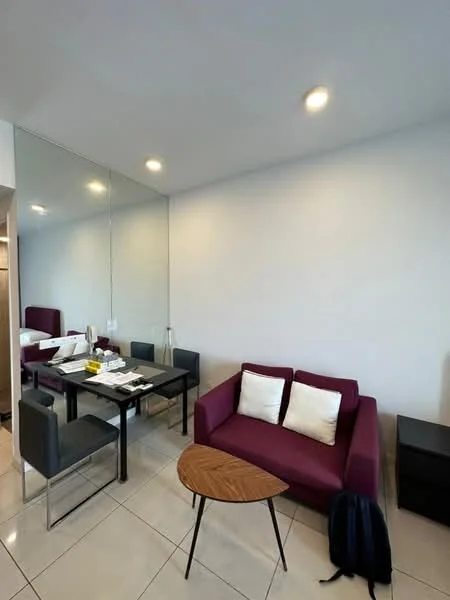 Living features: purple fabric sofa, 2 white throw pillows, glass dining table, 4 black dining chairs, wooden side table with black legs, mirror wall, recessed ceiling lights, cream tiled flooring; style: modern.