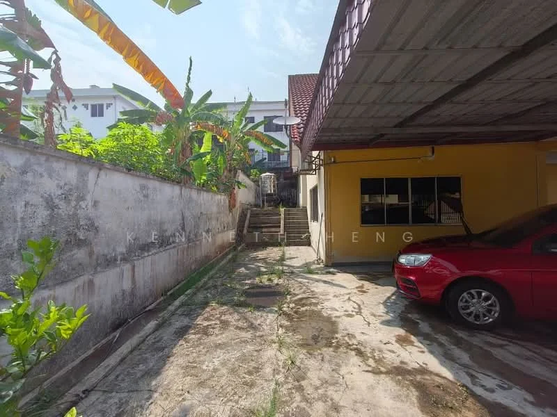 Exterior type: linked terrace house; features: concrete driveway, covered car porch, red sedan parked, mature banana plants, exposed brick wall, staircase leading to upper level, surrounding greenery, single-storey structure, metal roof, partially shaded area; style: modern.