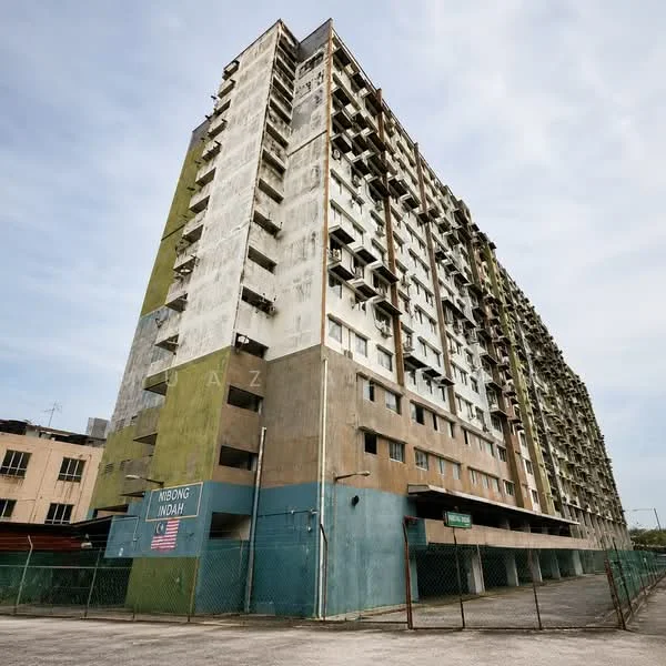 Exterior type: mid-rise condominium; features: weathered concrete facade, green and beige painted surfaces, balconies visible on multiple floors, exposed concrete structure, gated entry with fence, signage at the base of the building, parking area beneath the building, surrounding urban context; style: modern.