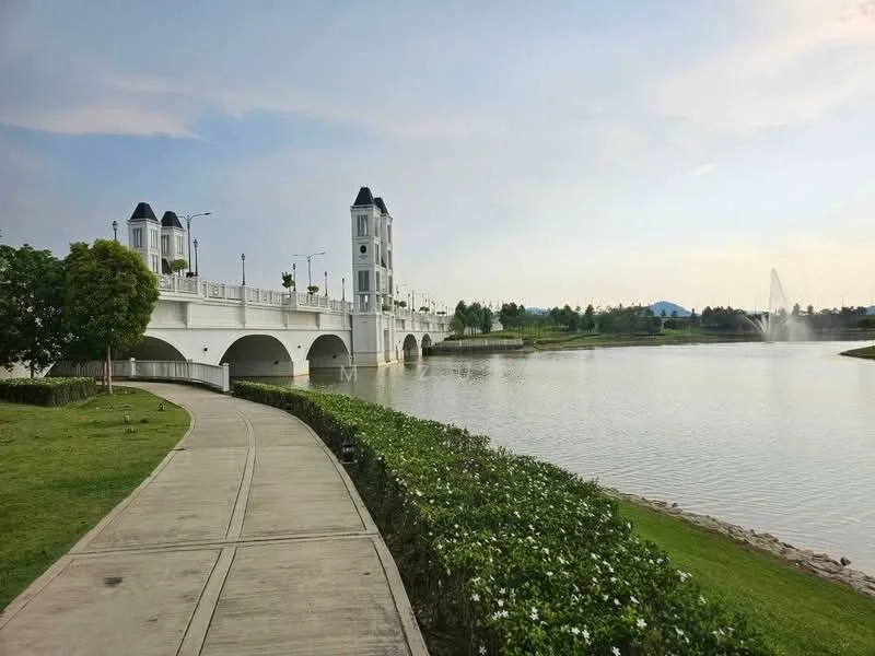 Exterior type: landscape garden; features: manicured lawn, pathway, waterfront view, decorative bridge, fountain in the lake, surrounding greenery, white railing, two towers with roofs, flower beds, clear blue sky; style: modern.