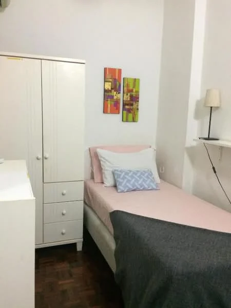 Bedroom features: single bed with pink bedding, decorative pillow with geometric pattern, white bedside lamp, white wardrobe with drawers, wooden flooring, two abstract paintings on the wall, shelf mounted on the wall; style: minimalist.